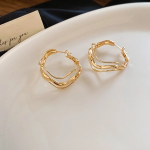 Detailed view of golden irregular wave circle earrings on a white decorative plate
