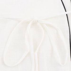 Detailed macro view of white linen apron with black trim and elegant tie-knot detail