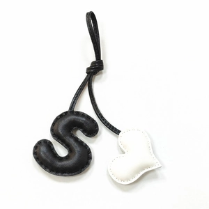 Detail of handmade leather bag charm featuring black S letter and white heart shape