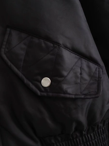 Detail of quilted pocket flap with silver button and elastic waist on black flight jacket