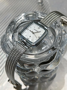 Macro view of a square quartz watch with a silver mesh strap and diamond markers