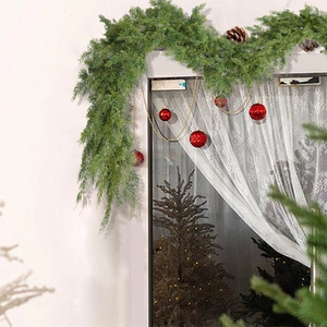 Green faux cedar Christmas garland with pine cones decorated on a white window frame