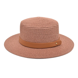 Detail of pink straw sun hat with leather band and gold buckle on white background