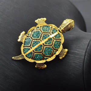 Detailed close up view of golden turtle brooch with green rhinestones luxury style pin