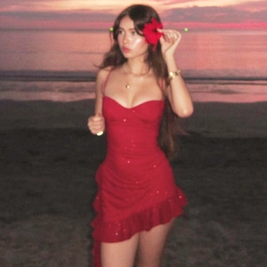 Detail of red sequined mini dress with ruffle hem and thin straps on a sunset beach