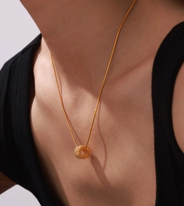 Detail of a gold-plated necklace featuring a pavé zircon cylinder charm on a model