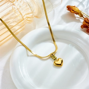 Gold heart pendant necklace with green stone on a snake chain against minimalist decor