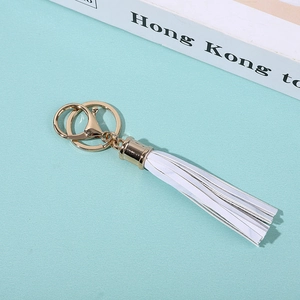 Detailed view of white PU leather tassel keychain with gold metal ring on green surface