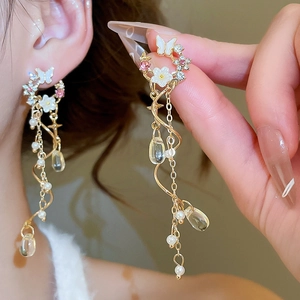 Macro shot of long gold tassel earrings with butterfly motifs and delicate pearls