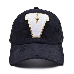 Close-up of distressed black mesh trucker hat featuring white plush V patch embroidery