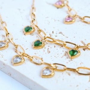 Close-up of gold heart pendant necklaces with green pink and white stones on stone