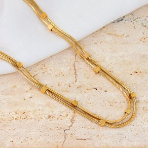 Close-up of golden double-layer snake chain necklace with cubic beads on silk background