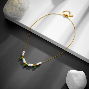 Detail view of a gold chain necklace with white pearls and square green gemstones