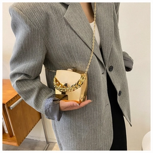 Detailed view of a gold metallic box clutch bag with elegant chain strap on a blazer
