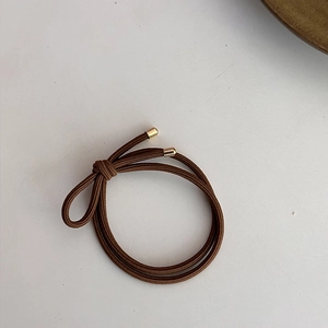 Détail d'un élastique à cheveux marron café avec fermoir en métal doré sur fond blanc