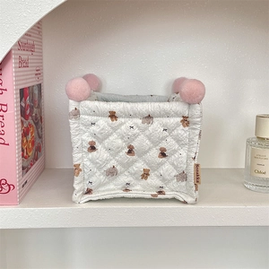 Close-up of quilted storage basket with bear patterns and pink pompoms on shelf