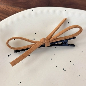 Detailed close-up of a brown suede bow hair clip on a white ceramic plate texture