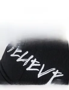 Detailed macro view of white BELIEVE letter embroidery on a black cotton baseball cap