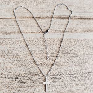 Macro shot of silver cross pendant with beaded chain on a light wood surface