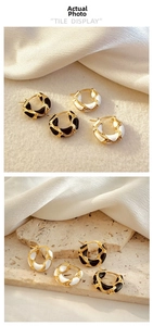 Detail showing 18K gold hoop earrings with black and white enamel wavy patterns