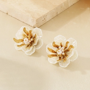 Detail of cream flower earrings with golden core and white pearls on stone background