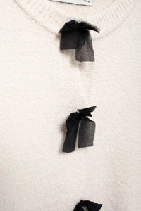 Close-up of white knit cardigan featuring black ribbon bows and soft wool texture detail