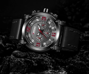 Detail of chronograph watch on dark stones showing red dial markers and leather strap