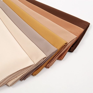 Close-up of stacked breathable matte satin square scarves in various earth tone colors