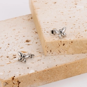Minimalist silver stainless steel dragonfly earrings placed on decorative travertine stone