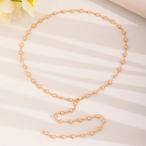Detail of gold Y-shaped necklace featuring elegant beige pearls with soft shadow lighting
