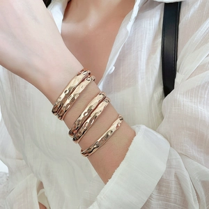 Detail of five rose gold hammered finish bracelets worn by a model on a white background