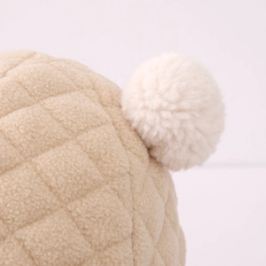 Makro-Detail von beige gestepptem Fleece-Stoff und einem weichen weißen Plüsch-Pompon