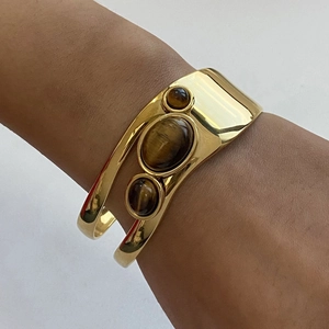 Detail of wide gold cuff bracelet featuring three vertical tiger eye stones on wrist