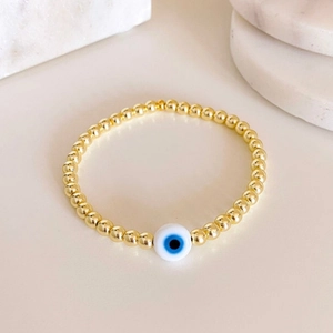 Gold-plated beaded elastic bracelet with Turkish evil eye charm on marble stand