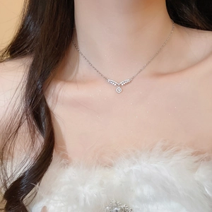 Détail du collier argenté avec ailes en V et pendentif en zircon sur le cou