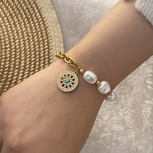 Detail of pearl and gold chain bracelet with a turquoise flower charm on a wrist