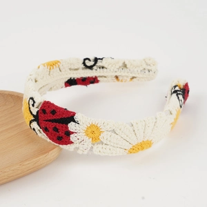 Detail eines handgehäkelten Stirnbands mit Marienkäfern und Gänseblümchen-Stickerei