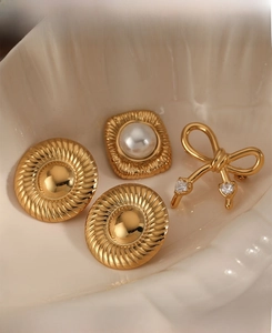 Détail de bijoux dorés avec nœud et perles sur un plateau en céramique en forme de coquillage