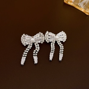 Detail of silver bow earrings with rhinestone tassels and white pearl accents on leather