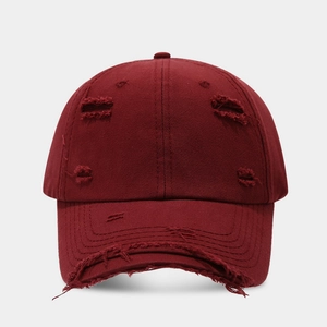 Close-up detail of distressed burgundy cotton baseball cap with ripped edges and holes