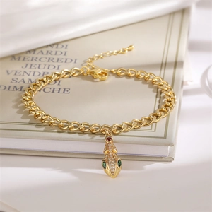 Detail of a gold-plated Cuban chain bracelet featuring a serpent head with green zircons