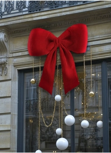 Detail view of large red velvet Christmas bow with gold chain and festive ornaments