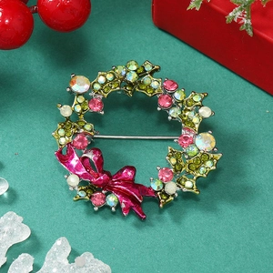 Close-up of Christmas wreath brooch with green leaves and pink rhinestone bow detail