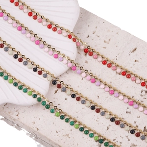 Colorful enamel bead necklace with golden chain on shell and stone background