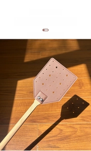 Detail of pink leather fly swatter head with star-shaped holes and long wooden handle