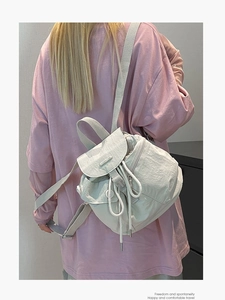 Minimalist beige nylon drawstring backpack with flap closure shown on a model outdoors
