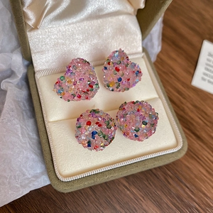 Detailed close-up of pink heart and round glitter stud earrings in a green velvet box