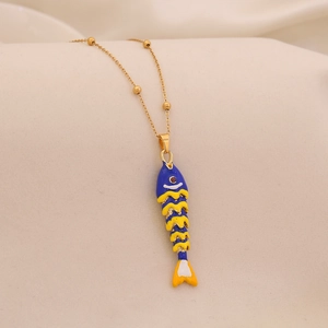 Macro shot of gold bead chain with blue and yellow enamel fish pendant on beige fabric