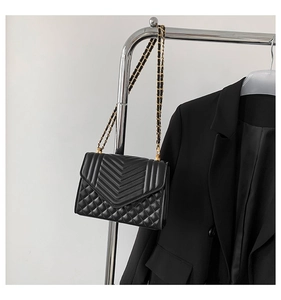 Detail of black quilted shoulder bag with V-shaped stitching and golden chain strap