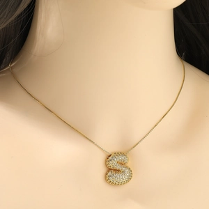 Detail of gold bubble letter S pendant necklace with shimmering zircon stones on mannequin